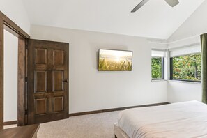 A bedroom with a large bed, a wooden door, a framed picture, and a window with a view of greenery. - The Willow at Treetop Villas (Lake Delton)