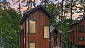 A modern wooden cabin with a staircase leading to a deck, surrounded by dense forest. - The Willow at Treetop Villas (Lake Delton)