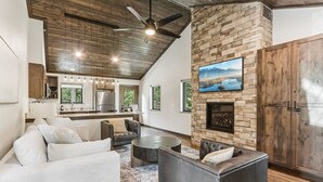 A modern living room with a stone fireplace, leather sofas, and a kitchen in the background. - The Willow at Treetop Villas (Lake Delton)