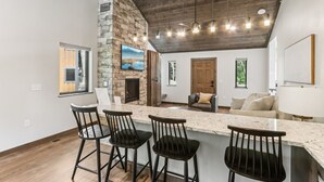 A spacious kitchen with a stone accent wall, a built-in fireplace, and a bar area with stools. - The Willow at Treetop Villas (Lake Delton)