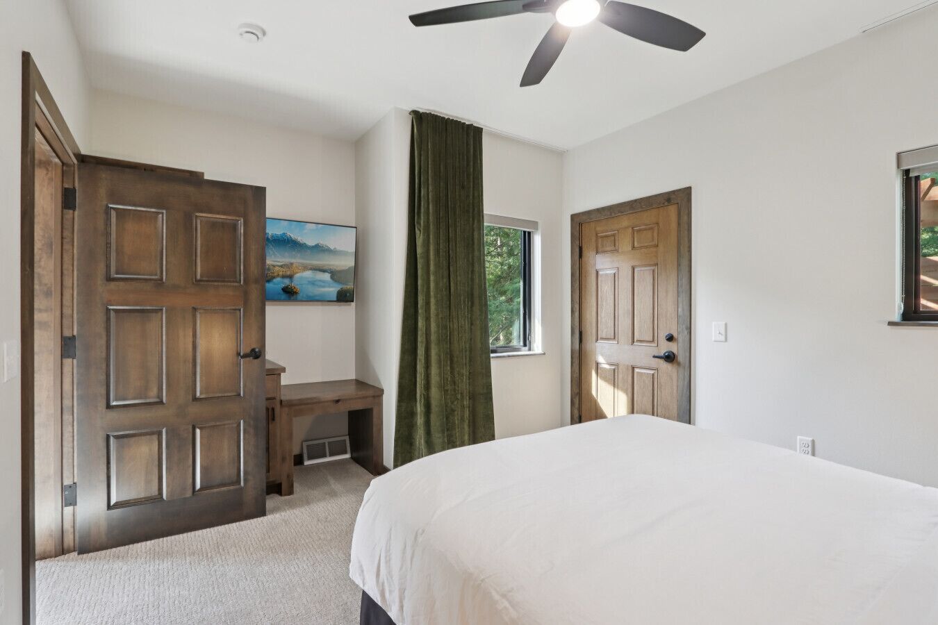 Une chambre à coucher avec un lit, un bureau, une fenêtre donnant sur un beau paysage et un ventilateur de plafond.