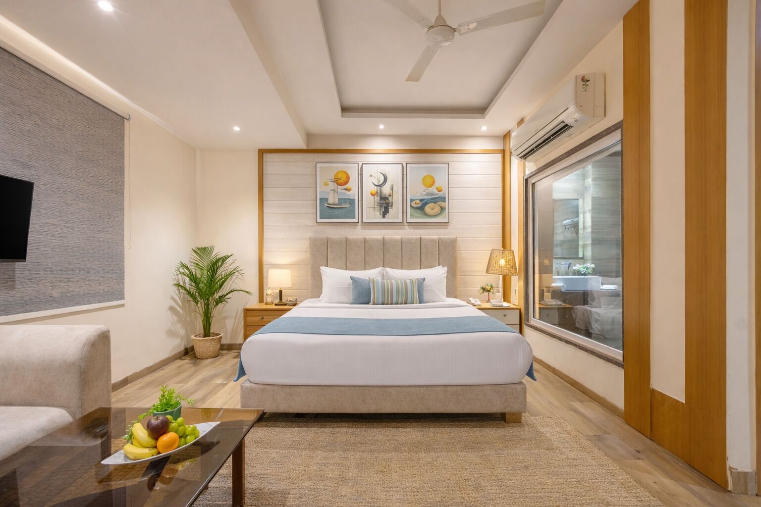 A modern hotel room with a large bed, a flat-screen TV, a ceiling fan, and a large window.