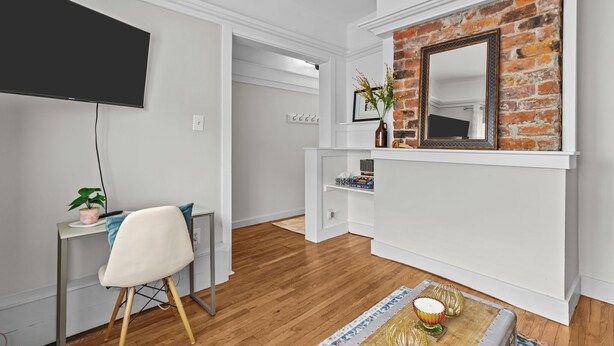 Ein modernes Wohnzimmer mit einem Flachbildfernseher, einem weißen Sessel, einem kleinen Tisch mit Dekorationsgegenständen, einer Ziegelwand als Blickfang und einem weißen Kaminumbau.