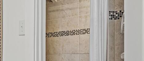 A shower area with beige tiles, a white shower curtain, and a wooden bench.