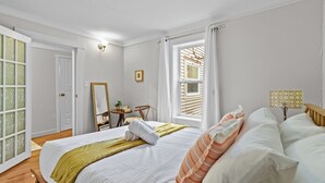 Ein Schlafzimmer mit Bett, Schreibtisch, Stuhl, Lampe und einem Fenster mit Vorhängen.
