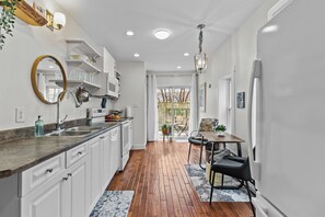 A modern kitchen with white cabinets, a wooden countertop, and a dining area with a table and chairs. - Stay on Bond 2BR Queen Deck Vws (St. John's)