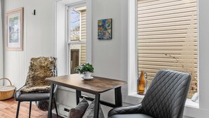 Ein modernes Wohnzimmer mit einem Holzesstisch, zwei Stühlen, einer Pendelleuchte und großen Fenstern mit Jalousien.