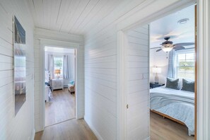 Un pasillo que conduce a un dormitorio con cama, ventilador de techo y ventana.