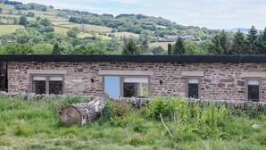 Un bâtiment en pierre doté de nombreuses fenêtres et d’une porte, entouré d’un mur de pierre et d’une zone herbeuse.