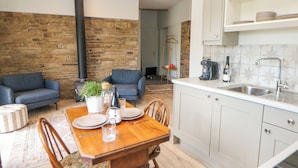Une cuisine moderne avec des meubles blancs, un coin repas doté d’une table et de chaises en bois, et un mur en pierre en arrière-plan.