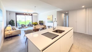 A modern kitchen with a central island, a dining area with a table and chairs, and a view of the outdoors through a large window. - Modern and bright apartment near Estepona beach and center (Estepona)