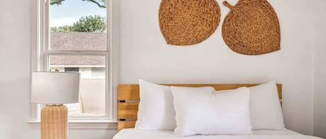 A bedroom with a bed, a nightstand with a lamp, and two woven wall decorations.