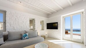 Un soggiorno moderno con una parete in mattoni bianchi, un divano grigio con cuscini, un tavolino in legno con una ciotola decorativa e una grande TV a parete.