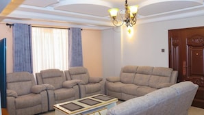 A living room with four beige sofas arranged around a central coffee table, a chandelier, and a wooden door. - Shirpelle Suites Kiamunyi (Nakuru)