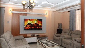 A modern living room with a flat-screen TV mounted on the wall, two sofas, a coffee table, and a chandelier. - Shirpelle Suites Kiamunyi (Nakuru)