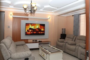 Una sala de estar moderna con un televisor de pantalla plana montado en la pared, dos sofás, una mesa de centro y una araña.