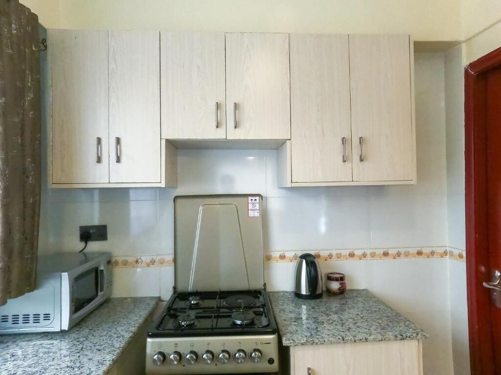 Uma cozinha com armários de madeira clara, fogão a gás, micro-ondas e um balcão pequeno.