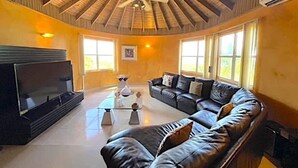 Un salon spacieux avec un grand canapé en cuir, un téléviseur à écran plat et un ventilateur de plafond.