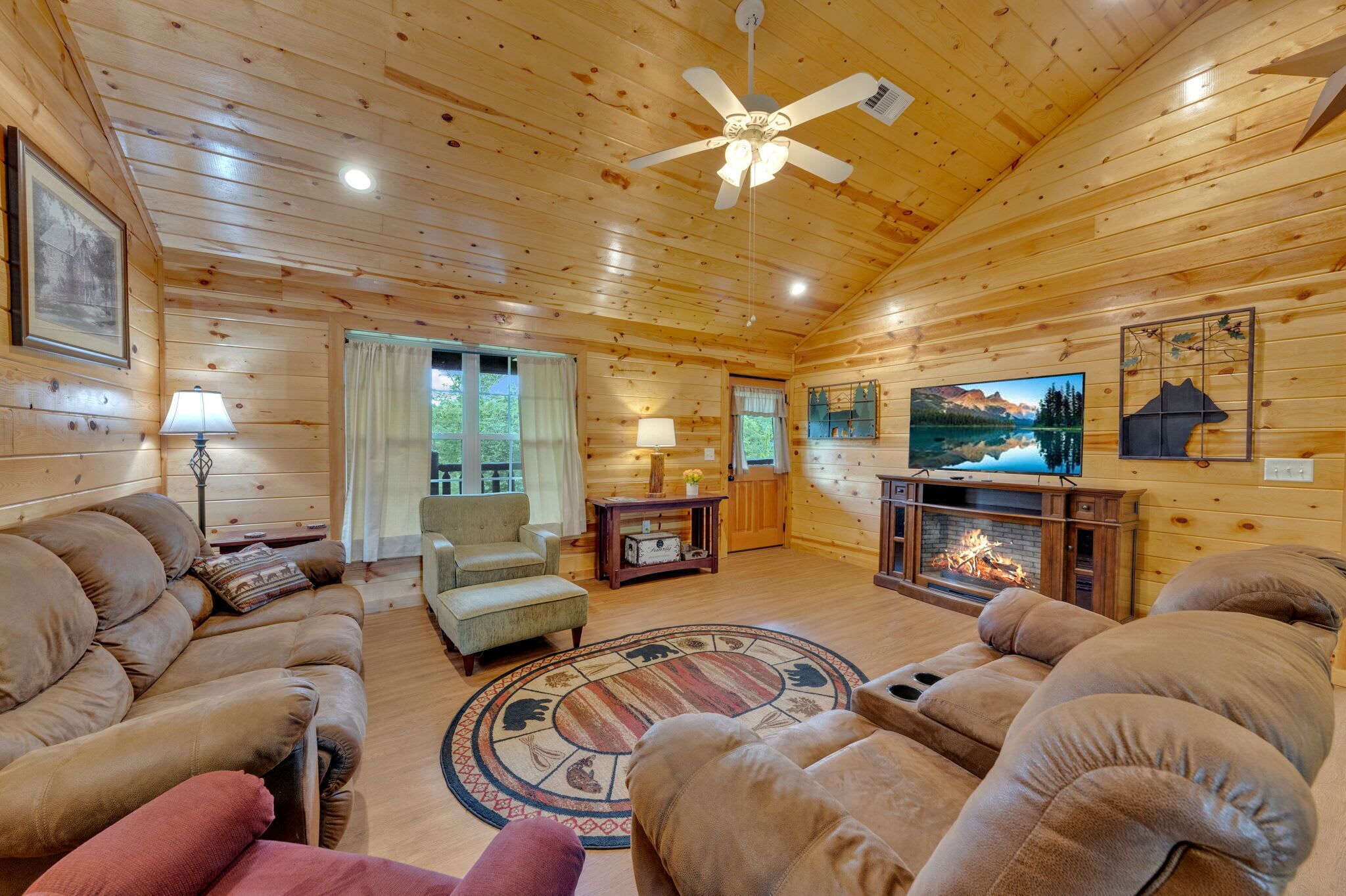 A cozy cabin interior with wooden walls, a fireplace, a television, and comfortable seating.