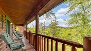 Une véranda en bois, dotée de fauteuils à bascule, qui offre une vue sur un paysage verdoyant et luxuriant.