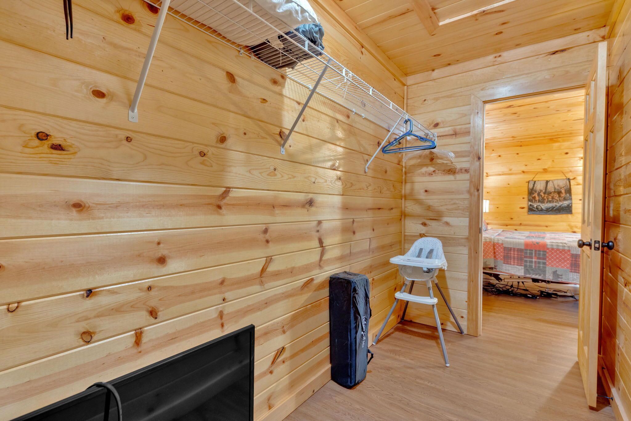 Interno di una baita in legno con un letto, un piccolo angolo salotto, un camino e uno scaffale in metallo con vestiti.