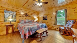 Une chambre confortable dans un chalet en rondins, avec un lit, un fauteuil à bascule, un banc en bois et un ventilateur de plafond.