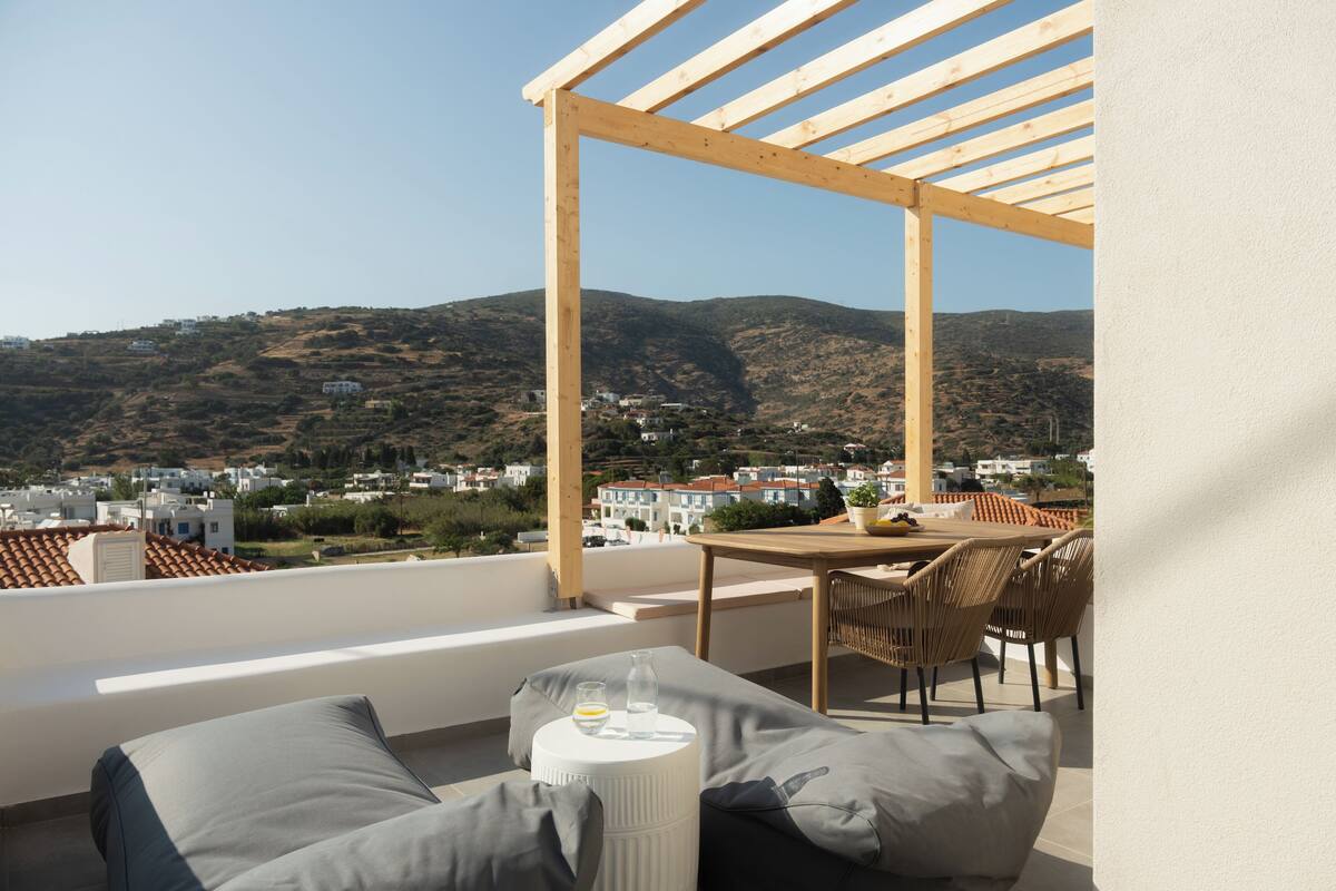 A balcony with a wooden pergola, a table, and chairs.