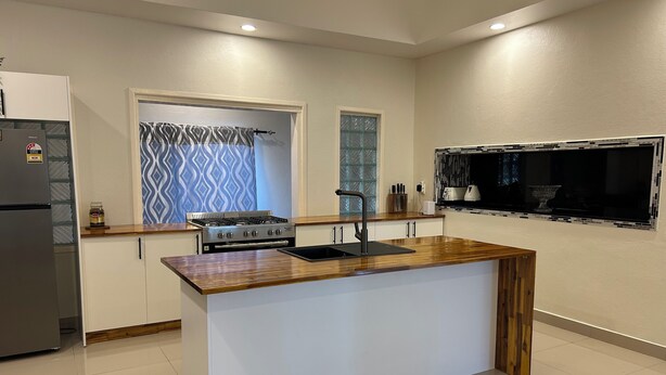 A modern kitchen with a central island, built-in appliances, and a window with patterned curtains.