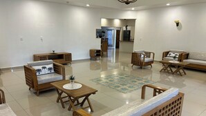 A spacious living area with wooden furniture, including sofas and chairs, a coffee table, and a tiled floor.