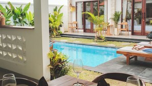 Un área de comedor con vista a la piscina, mobiliario exterior y un balcón con barandilla.