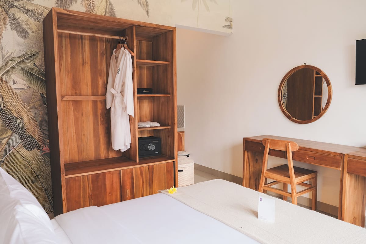 Een slaapkamer met een houten garderobe, een bureau, een stoel en een ronde spiegel aan de muur.