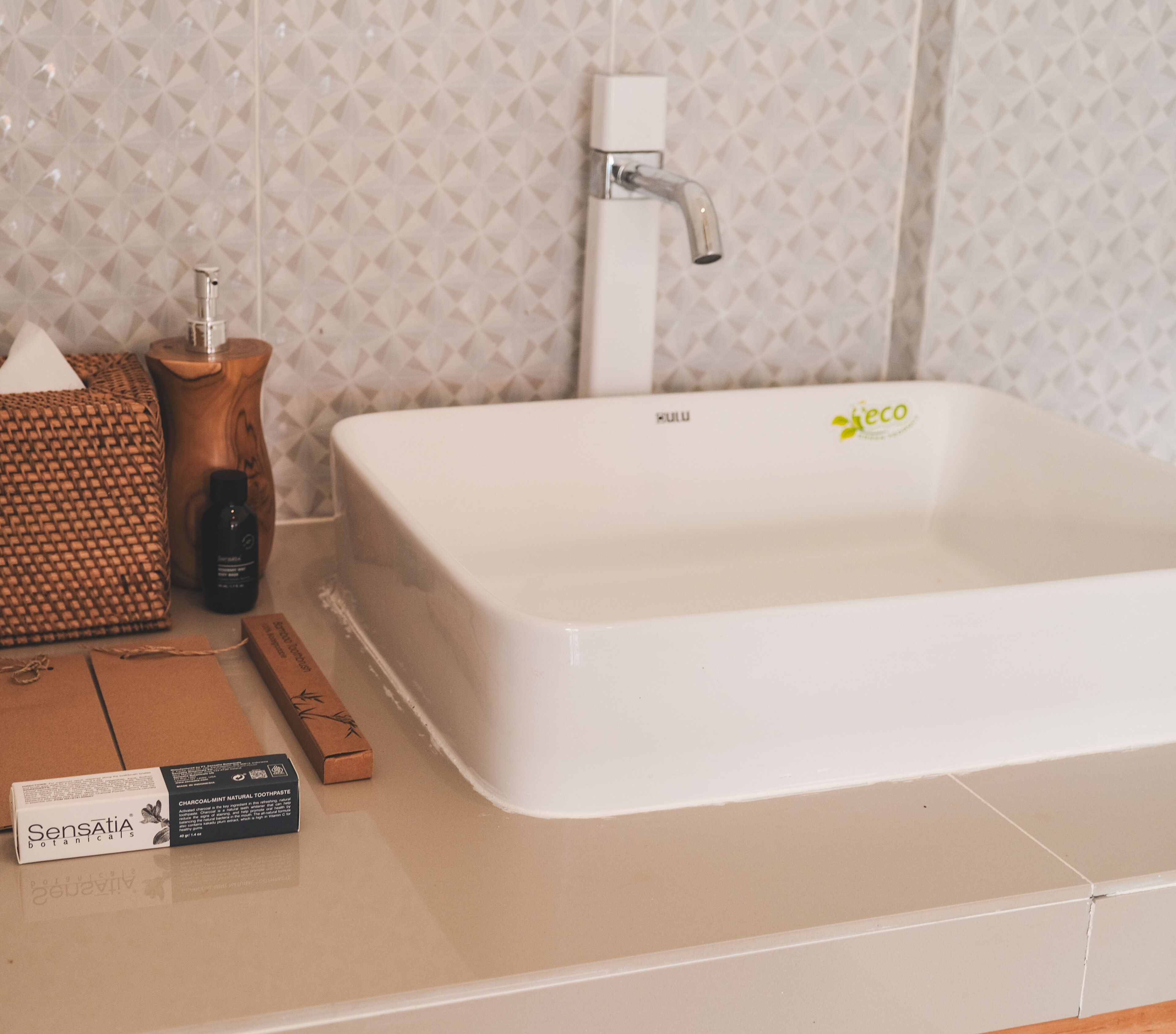 A bathroom with a white bathtub, a wooden side table, a bottle of soap, and a box of Sensatia Botanicals toothpaste.