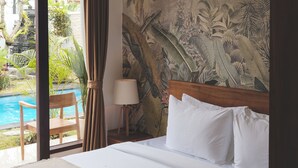 Habitación de hotel con cama, mesita de noche, lámpara, vista a una piscina y un mural tropical en la pared.