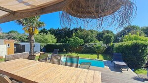 A wooden deck with a pool, lounge chairs, and a hanging basket. - House with heated pool Soulac 4bed near Ocean (Soulac-sur-Mer)