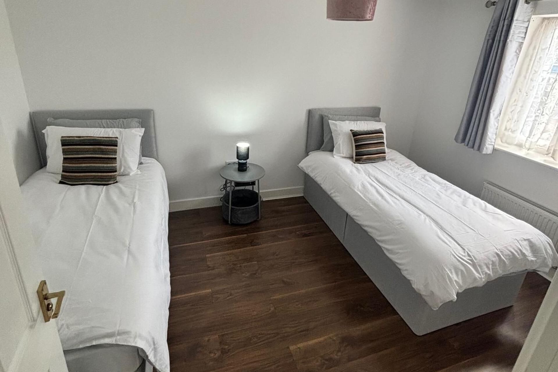 A room with two single beds, a small round table with a lamp, and a radiator.