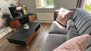 A modern living room with a grey sofa, a black coffee table, and a television on a wooden stand. - Trowbridge House, Long Stay Disc, Parking, Wifi (Swindon)