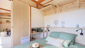 A bedroom with a bed, a hat on the bed, and a wall with a shelf and two wine glasses. - CHALET YOPLANI - UNDER THE CORSICAN SUN 6 PEOPLE (Sorbo-Ocagnano)