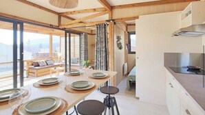 A modern kitchen with a large island, wooden beams, and a dining area with a table set for four. - CHALET YOPLANI - UNDER THE CORSICAN SUN 6 PEOPLE (Sorbo-Ocagnano)