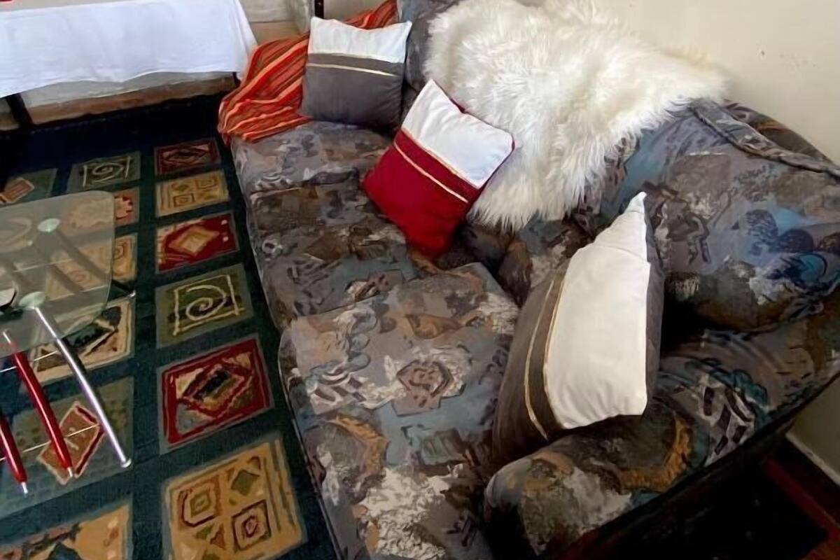 Ein Zimmer mit einem gemusterten Teppich, einem Sofa mit vielen Kissen, einem kleinen Tisch mit weißer Tischdecke und einem dekorativen Gegenstand auf dem Tisch.