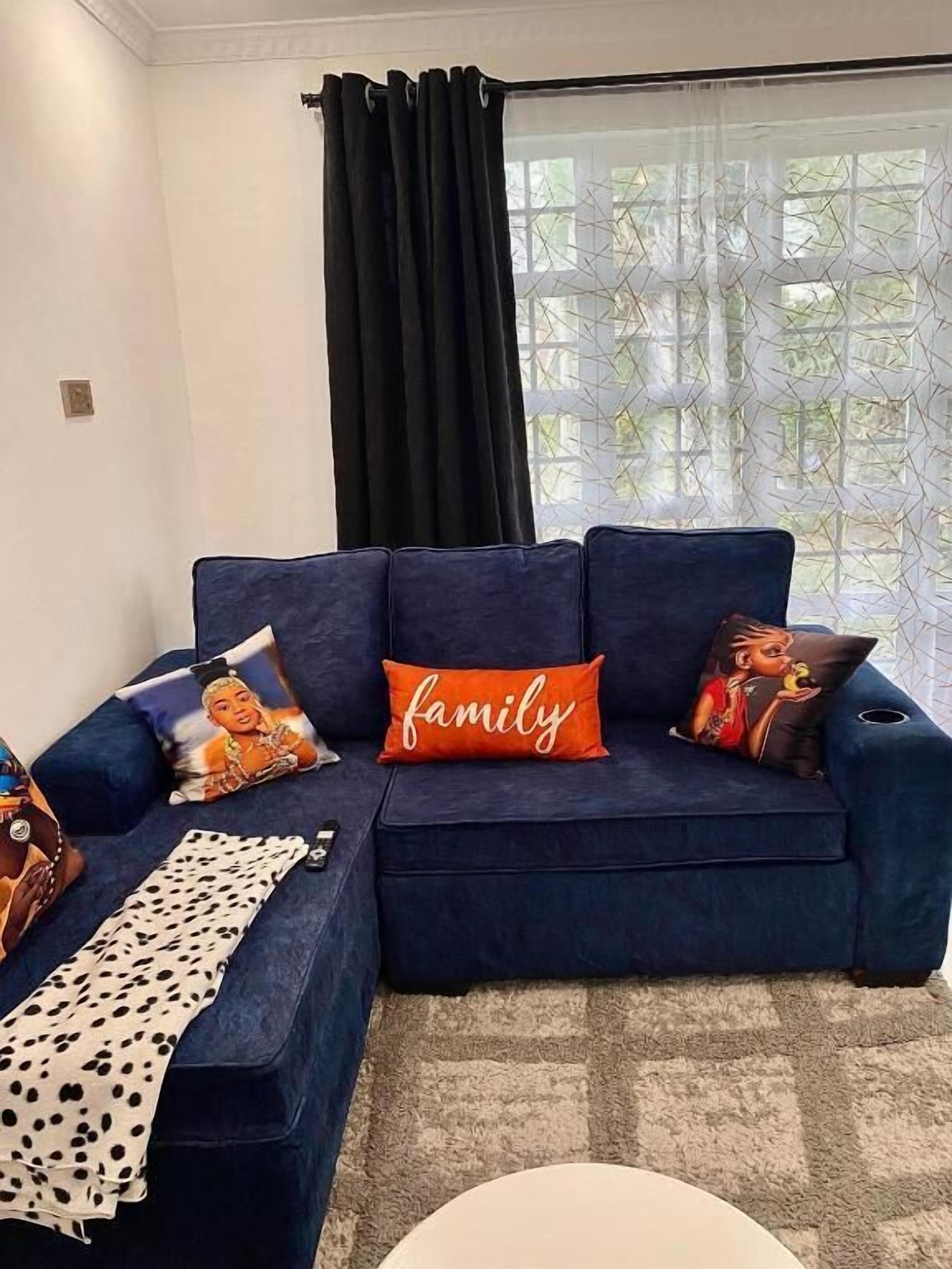 A dark blue sofa with three pillows, one with the word "family" and another with a child. A polka-dotted throw is draped over the sofa.