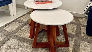 Un salon avec deux petites tables rondes blanches, un canapé bleu, un tapis à motifs et un téléviseur diffusant un paysage de montagne.
