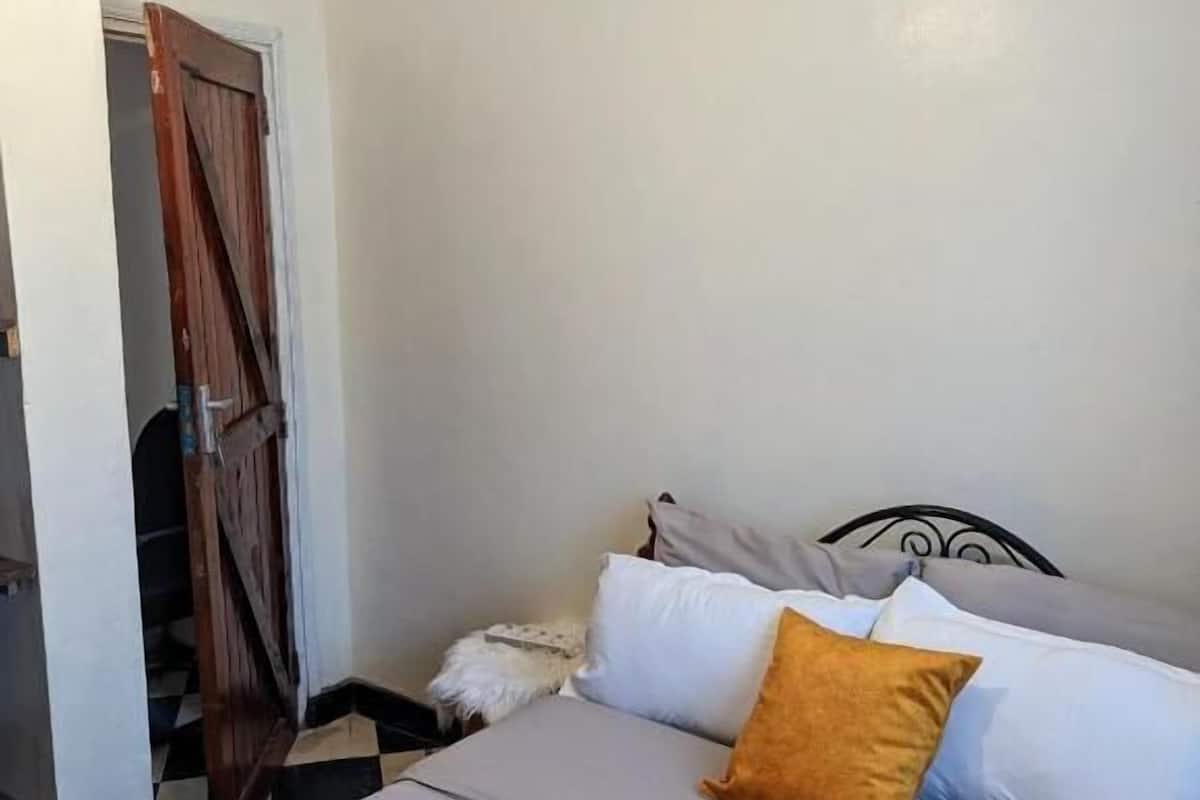 Ein Schlafzimmer mit Bett, Kissen, einem Nachttisch und einer Holztür.