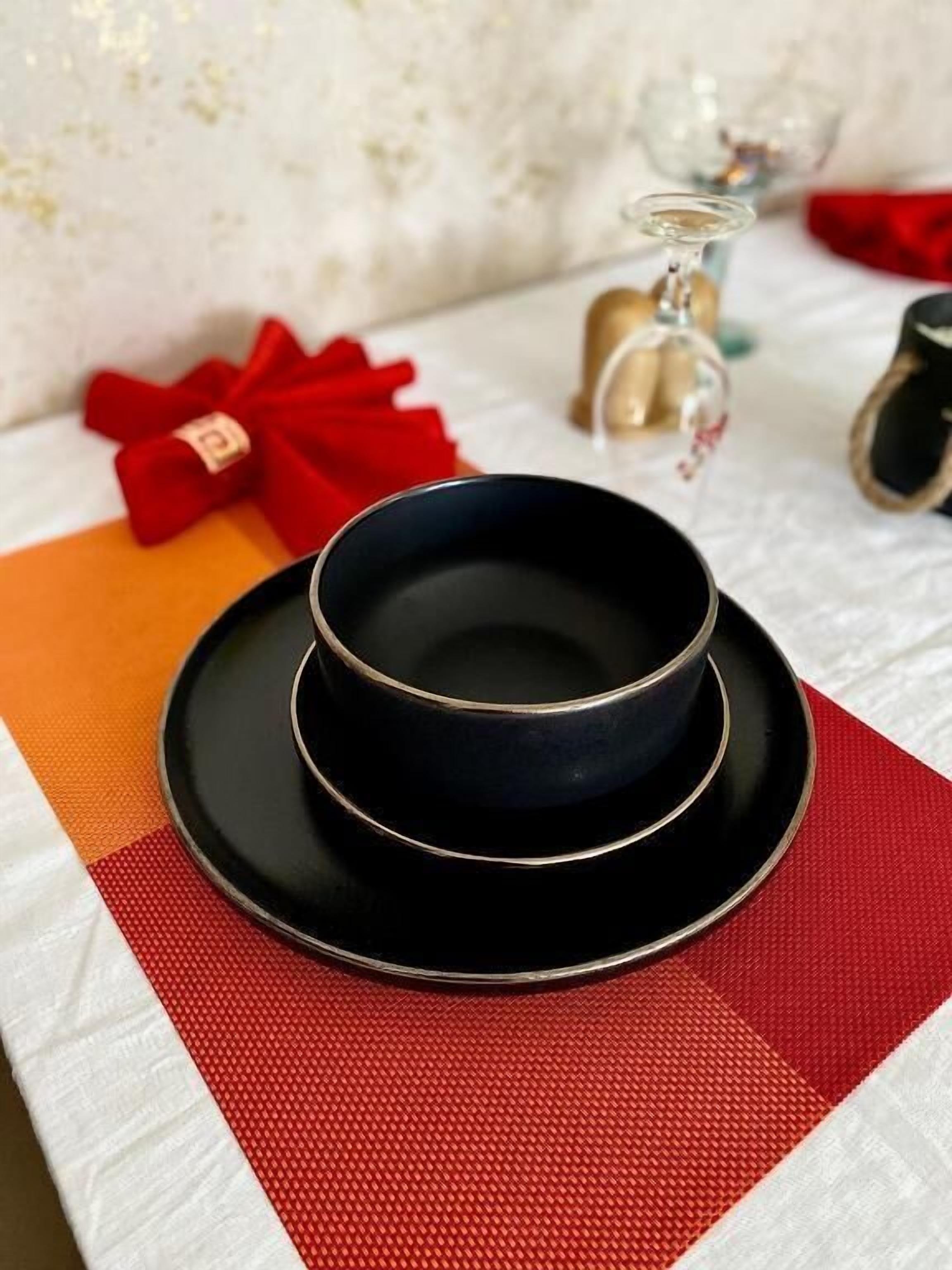 Une table dressée avec un bol noir sur une assiette noire, une serviette rouge et un ruban rouge sur une boîte cadeau.