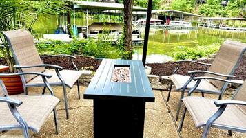 An outdoor seating area with a table and chairs, surrounded by a garden and a body of water.