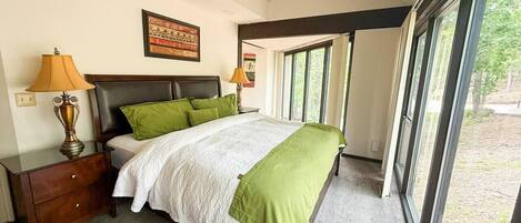A bedroom with a bed, nightstands, lamps, a framed picture, and large windows.