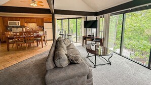 Un salon spacieux doté d’une grande fenêtre, d’un canapé, d’un téléviseur et d’un coin repas avec des meubles en bois.
