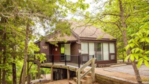 A cabin with a wooden deck, a staircase, and a number '102' on the door. - Treetop Village Treetop Escape #102-3BD/3BA/Pools/Grill/Dock/Deck-6PP (Village of Four Seasons)