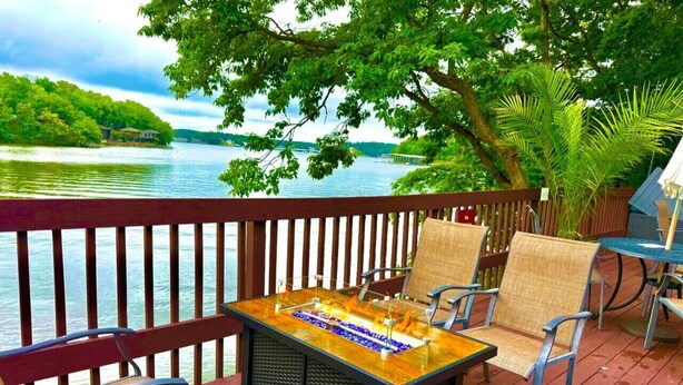 A deck with a glass-top table and chairs, overlooking a body of water and a distant shoreline. - Treetop Village Willow Waters Escape#110-3BD/3BA/Pools/Deck/Dock/Grill-6PP (Village of Four Seasons)