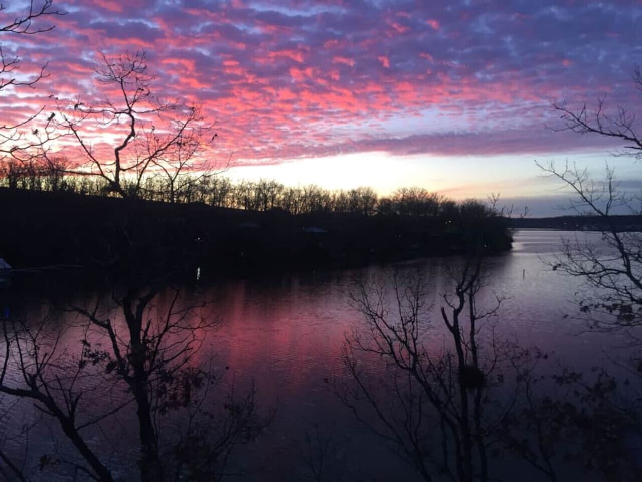 A serene lakeside view with a sunset sky reflected on the water, surrounded by trees.