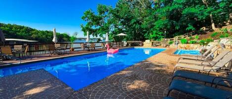 A swimming pool with a pink flamingo float, surrounded by lounge chairs and a brick patio.